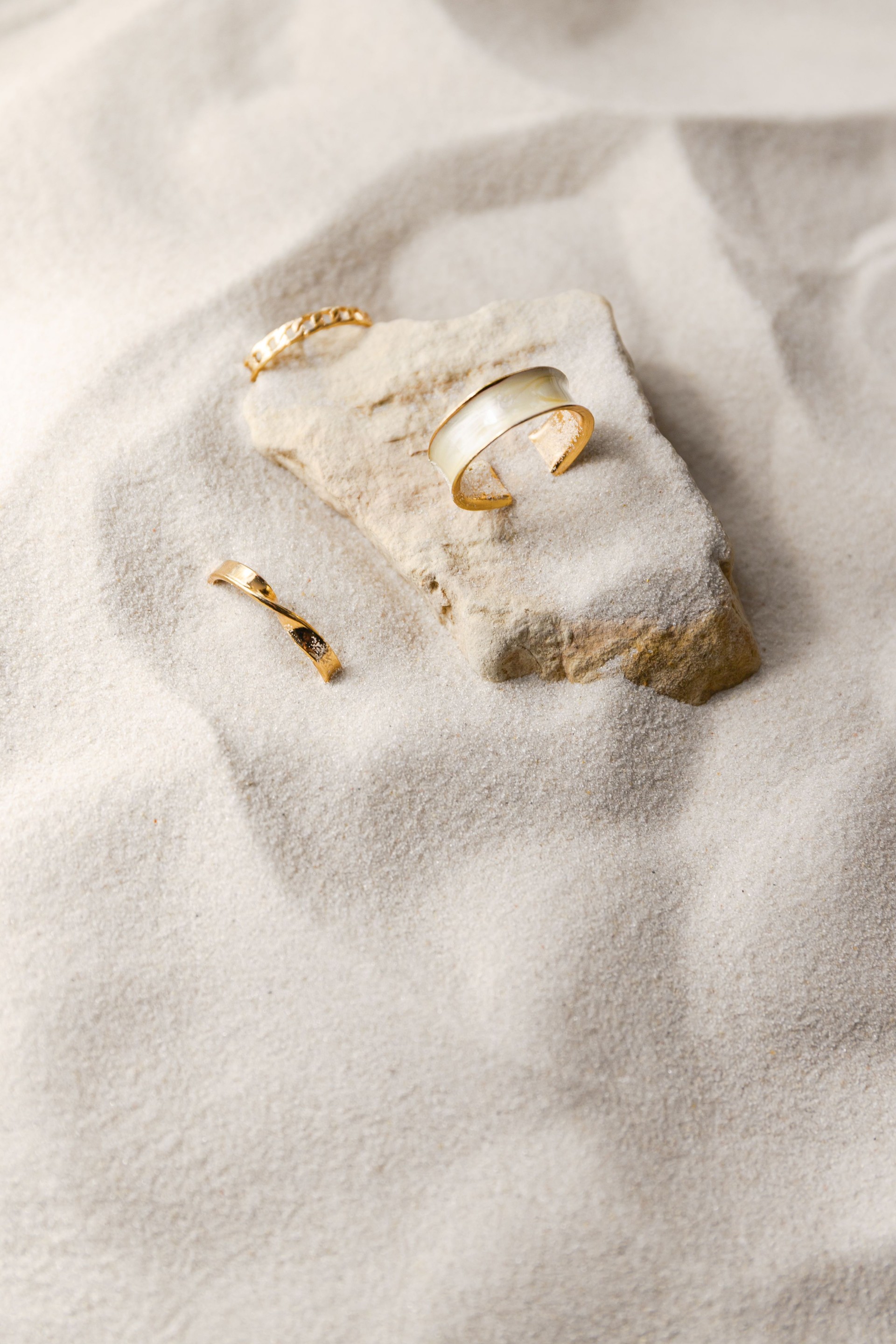 Creative still life with golden rings on a nature sand and stone background
